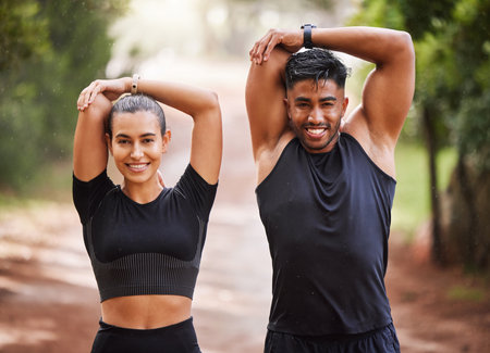 Fit couple or active, athlete friends stretching arms for exercise warmup outdoors in forest. Workout partners or smiling joggers about to run or do cardio training for health and wellness lifestyle.の写真素材