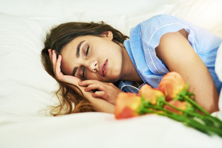 Shell wake up to a nice surprise. an attractive young woman asleep beside some flowers in her bed.の写真素材