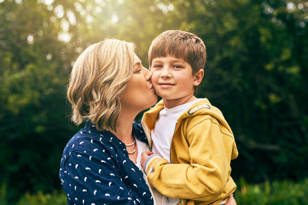 I will never stop loving you. a mother kissing her son on the cheek outside.の写真素材