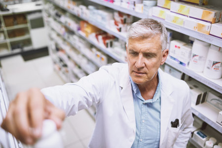 This shouldnt be here. a focused mature male pharmacist putting a medication bottle back on the shelf in a pharmacy.の写真素材