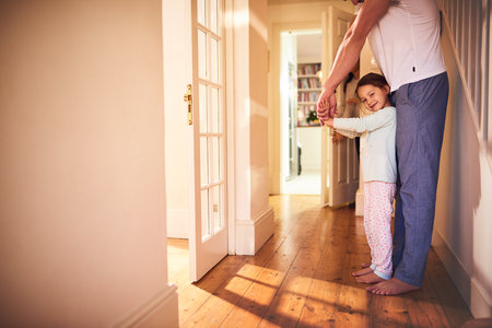 I want to be as big as daddy. Portrait of a cheerful little girl playing around the house with her dad while she looks at the camera at home.の写真素材