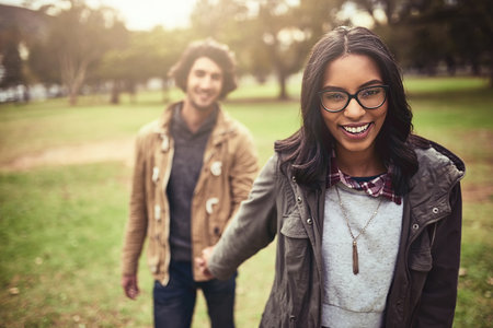 Come follow me. Portrait of an cheerful young couple walking and holding hands while looking at the camera outside in a park.の写真素材