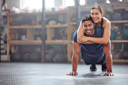 Fitness couple having fun while man does push ups and exercise together at the gym. Healthy, fit and athletic friends playing and silly while enjoying training session with teamwork at a health clubの写真素材