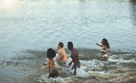 Swimming, fun and freedom in the sea with a group of young friends taking a swim in the ocean by the beach while on holiday or vacation. Diverse people playing, bonding and feeling carefree togetherの写真素材