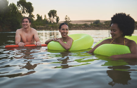 Fun group of diverse friends relaxing in lake water, enjoying nature and bonding on a getaway vacation in the countryside together. Happy men and women laughing, smile and looking relaxed on holidayの写真素材
