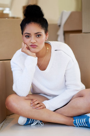 I miss my old home already. Portrait of a young woman sitting on her own while surrounded by cardboard boxes.の写真素材