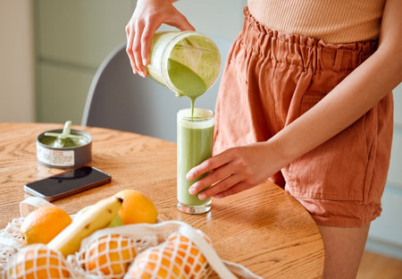 Closeup of a female pouring green healthy smoothie to detox, drinking vitamins and nutrients. Woman nutritionist having a fresh fruit juice to cleanse and provide energy for healthy lifestyleの写真素材