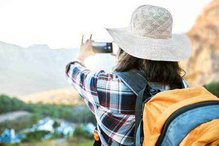 Hiking woman taking photo on adventure with phone in nature, making memories on hike and enjoying the beautiful view in the countryside on vacation. Person taking pictures of the natural environmentの写真素材