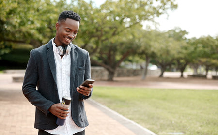 Young, cool smiling businessman on a phone having a walk in the park outside in nature. Happy man texting, chatting or reading messages on a smartphone outdoors on a break from work, over copy space.の写真素材