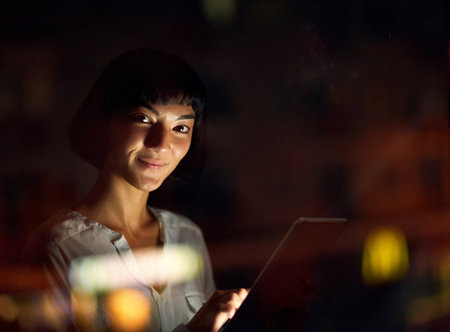 My internet provider keeps me connected all night long. a young businesswoman using a digital tablet during a late night at work.の写真素材