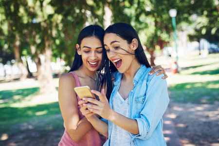 I cant believe he sent that. two young friends using a phone together outdoors.