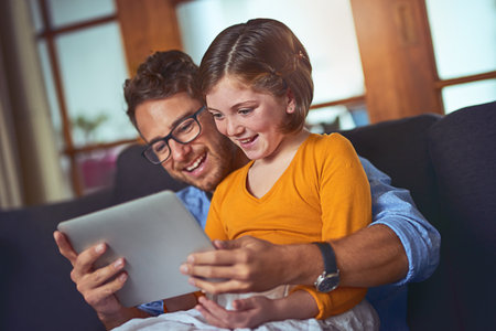 Raising a smart little girl. a father and daughter using a digital tablet together on the sofa at home.の写真素材