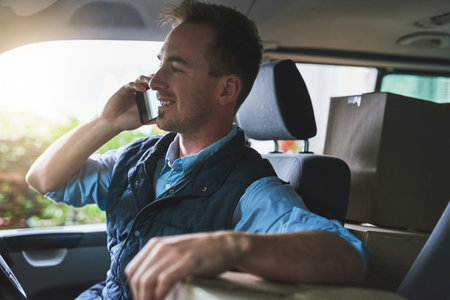 Im on my way with your package. a courier talking on a cellphone while sitting in a delivery van.