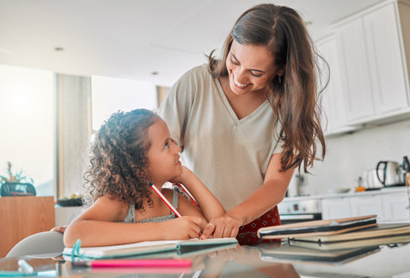 Homeschool, learning and bonding with a mother and daughter doing homework in the kitchen at home. Happy parent helping her child with a school task, smiling, talking and enjoying time togetherの写真素材