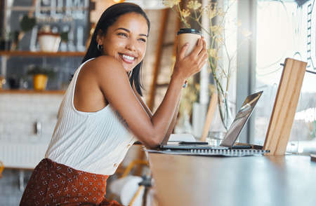 Happy woman relaxing in a coffee shop with a smile and thinking. Female enjoying relaxed day alone working on a laptop while browsing the internet and social media and having an startup project ideaの写真素材