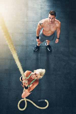 Channel the fighter within and keep going. a young woman climbing a rope with a man in the...