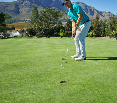 This is going straight in. a focused young man hitting a golfball with a putter into a hole on a...