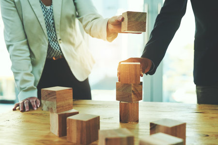 Laying their success on a solid and stable foundation. two unrecognisable businesspeople stacking wooden blocks together in an office.の写真素材