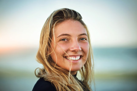 The ocean air makes me smile. Cropped portrait of an attractive young female surfer standing on the...