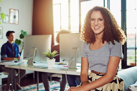 Were determined to transform the creative landscape. Portrait of a young designer sitting in an office with her colleagues in the background.の写真素材