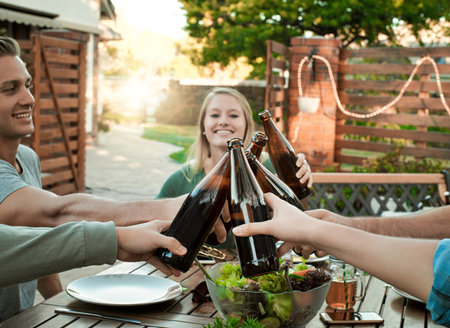 Celebrating our friendship. a group of young friends holding up drinks and toasting outside around a table to celebrate their friendship.の写真素材