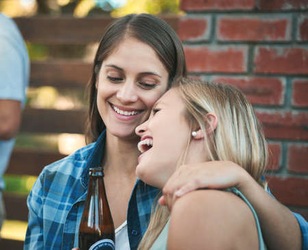 Fun times, thats what friends are for. two happy young women enjoying some beers at a get together with their friends.の写真素材