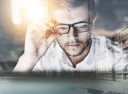 Hes got great visions for the city. Multiple exposure shot of a young businessman adjusting his spectacles superimposed over a cityscape.の写真素材