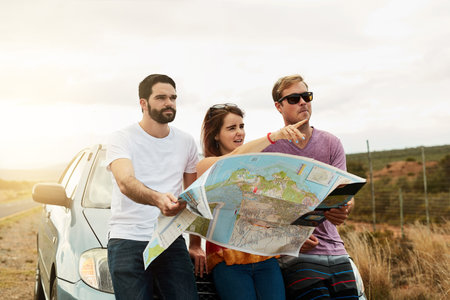 Road trip time. a group young friends holding a road map and planning where to go while standing...