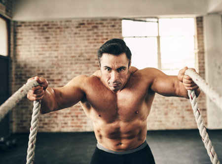 These ropes are nothing to me. a fit and determined young man making use of ropes to workout in the...