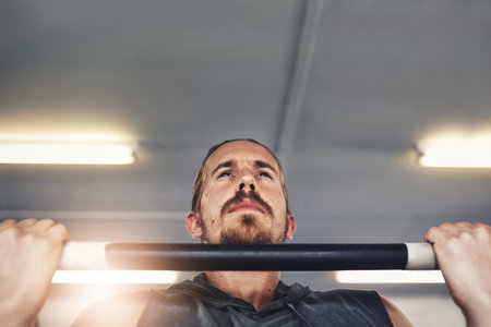 Focus on what you could gain in the end. a young man doing pull ups in a gym.