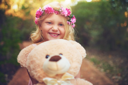 Were both smiling for the camera. a happy little girl holding a teddy bear and looking at the camera while standing in the middle of a dirt road.の写真素材