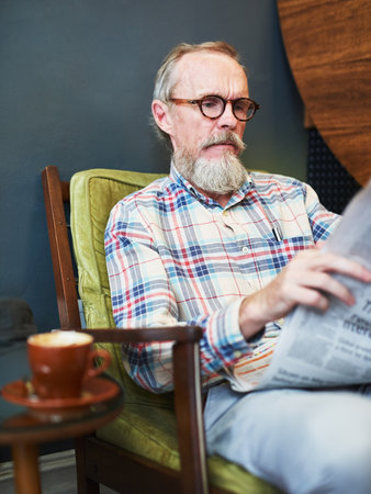 Coffee and newspaper, how I love to start my afternoons. a senior man reading the newspaper and having coffee at a coffee shop.の写真素材