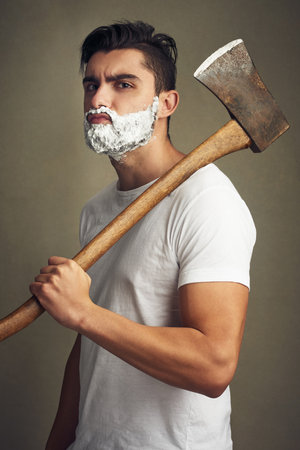 When a blade just wont do. a handsome young man shaving his beard with a lumberjack.