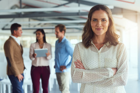 Im proud to be a part of this team. Portrait of a confident businesswoman posing in the office while her colleagues brainstorm in the background.の写真素材