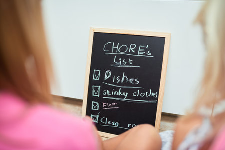 Time for chores. Rearview shot of two little girls looking at a list of chores on a chalkboard at home.の写真素材