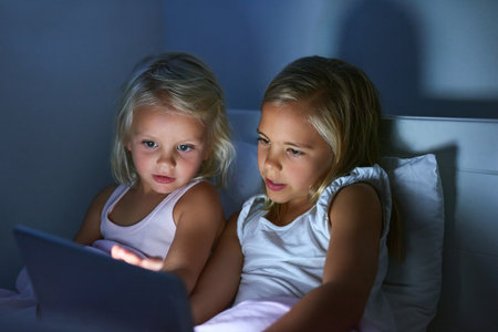 Playing on their favourite apps. two little girls using a digital tablet before bedtime.の写真素材