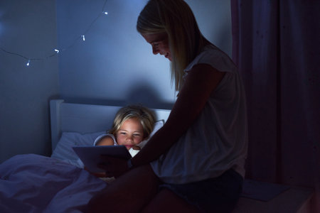 Just one more story. a little girl and her mother using a digital tablet before bedtime.