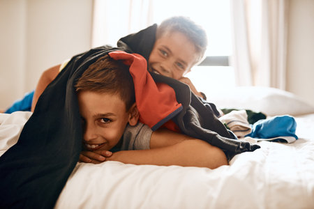 Silly moments. Portrait of two little brothers lying on a bed under a pile of laundry at home.の写真素材