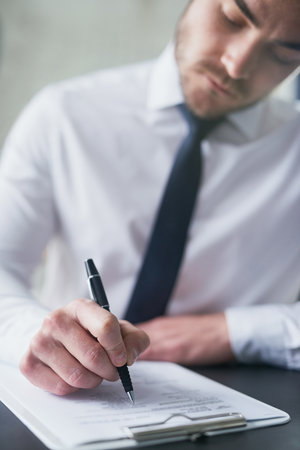 Hes well prepared for this questionnaire. a young businessman filling out paperwork on a clipboard while sitting at a table in an office.の写真素材