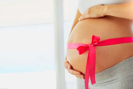 Lady in waitingfor her little princess. a pregnant woman with a pink ribbon tied around her belly.