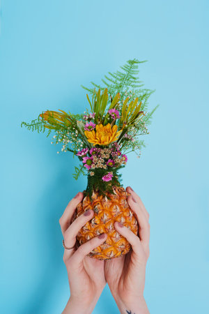 The earth laughs in flowers. an unrecognizable woman holding a pineapple stuffed with flowers.の写真素材