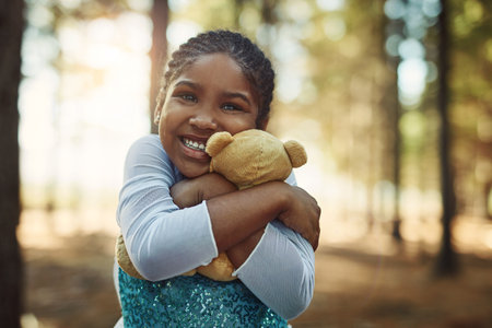 Cuddles for her fluffy little friend. Portrait of a little girl playing in the woods with her teddybear.の写真素材