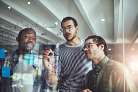 Plan first, act later. a group of young designers planning on a glass board.