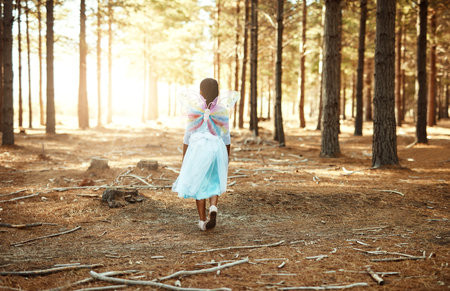 Fluttering through the forest. Rear view shot of a little girl walking in the woods while dressed up as a fairy.の写真素材