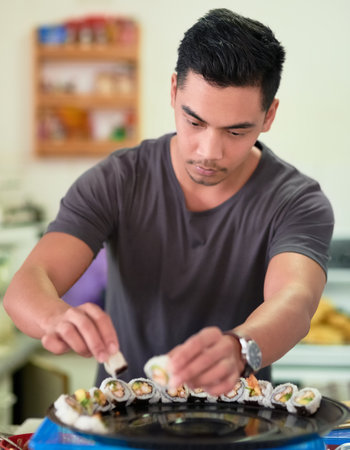 When it comes to sushi, hes a perfectionist. a young man arranging sushi on a platter at home.の写真素材