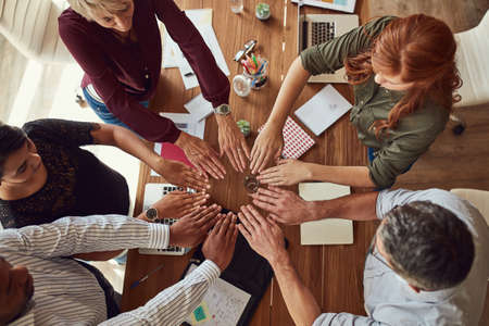 All hands on deck to get things done. High angle shot of a group of colleagues joining their hands in solidarity during a meeting in a modern office.の写真素材