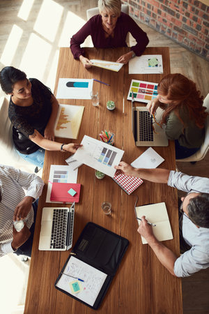 Working in a cooperative environment. High angle shot of a group of colleagues having a meeting in a modern office.の写真素材
