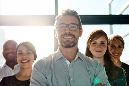 Were committed to delivering excellence. a businessman posing with his arms crossed with his colleagues in the background.の写真素材