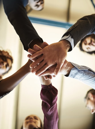 Unity makes them unstoppable. Low angle shot of a team of businesspeople piling their hands on top of each other in the office.の写真素材