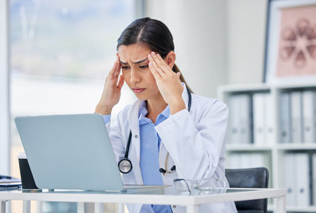 Stress or burnout with doctor thinking and working on laptop in hospital consulting room or office. Medical healthcare worker or specialist surgeon with anxiety headache from mental health issuesの写真素材